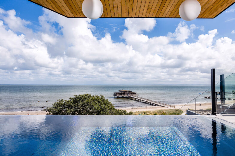 Infinitypool i solsken på rooftop spa med utsikt över strand och hav.